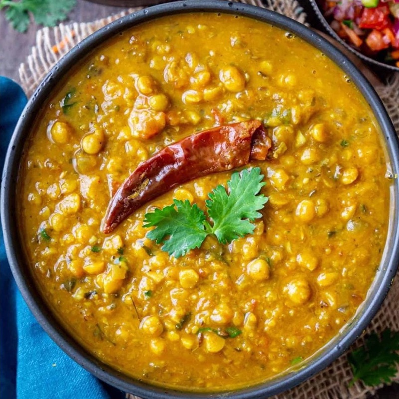A bowl of daal channa, thick and golden, with a whole dried red chilli and fresh coriander on top