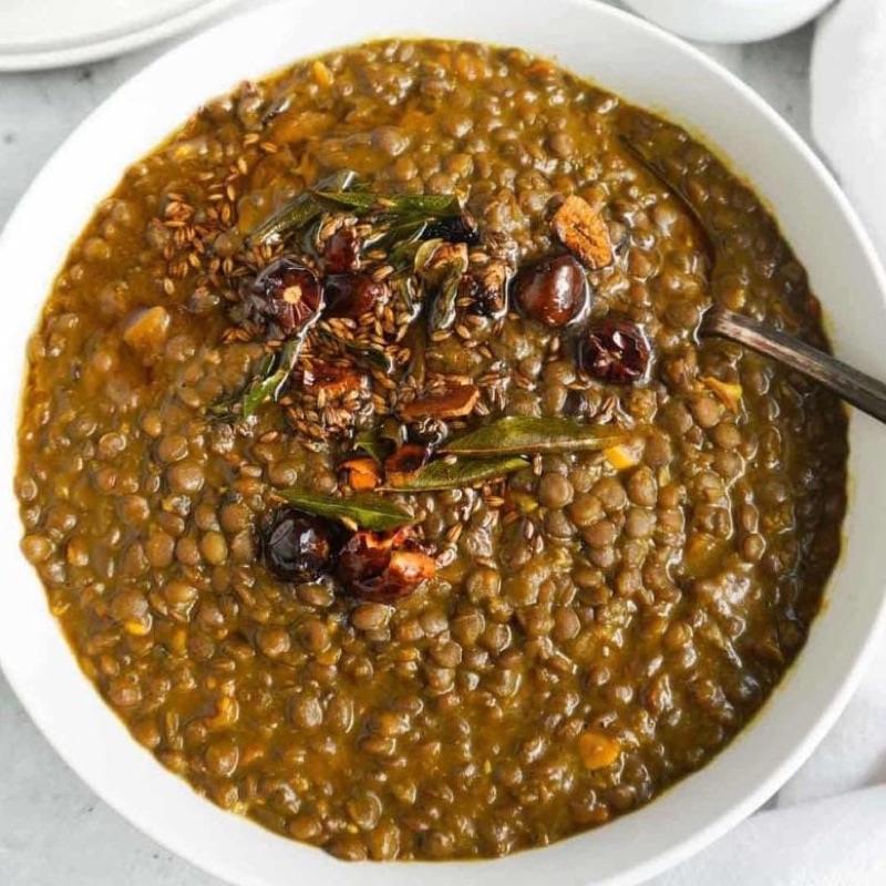 A bowl of daal kaali masar, whole brown lentils in a dark gravy, tempered with cumin, curry leaves and dried red chillies