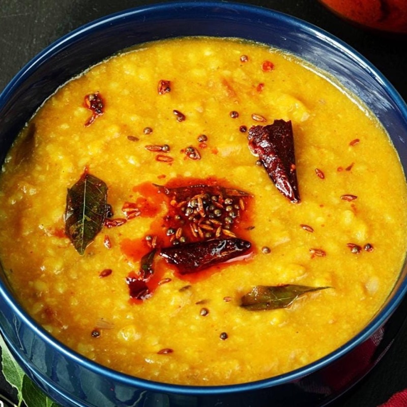 A bowl of daal moong masoor, bright yellow and soft, under a tarka of mustard seeds, cumin, bay leaf and dried red chillies